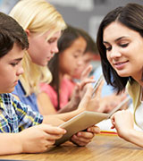 Teacher who is taking Learning and Teaching for a K-12 Digital Classroom Certficate courses assisting a student with a mobile (iPad, tablet) device