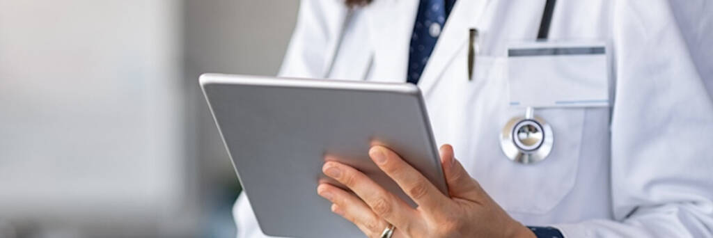 The image features a close-up of a healthcare professional, partially visible, holding a tablet. The person is dressed in a white lab coat with a stethoscope around the neck, symbolizing their medical role. This visual focuses on the use of technology in healthcare, illustrating a modern approach to medical practices and patient management. The clean and professional aesthetic emphasizes the precision and high standards expected in healthcare jobs. This image is suitable for an article discussing careers in the healthcare sector, particularly highlighting roles that integrate technology and clinical expertise.