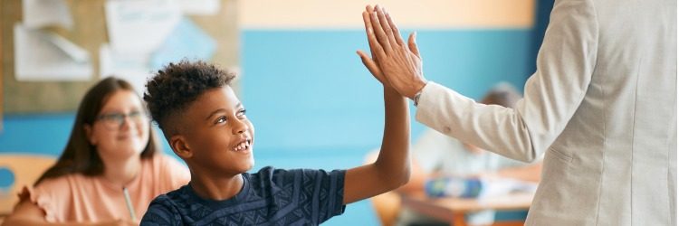 Student high-fiving his teacher in a classroom