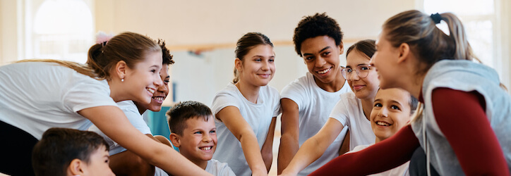 Female-coach-and-group-of-students-gathering-their-hands-in-unity-on-physical-education-class-at-school.