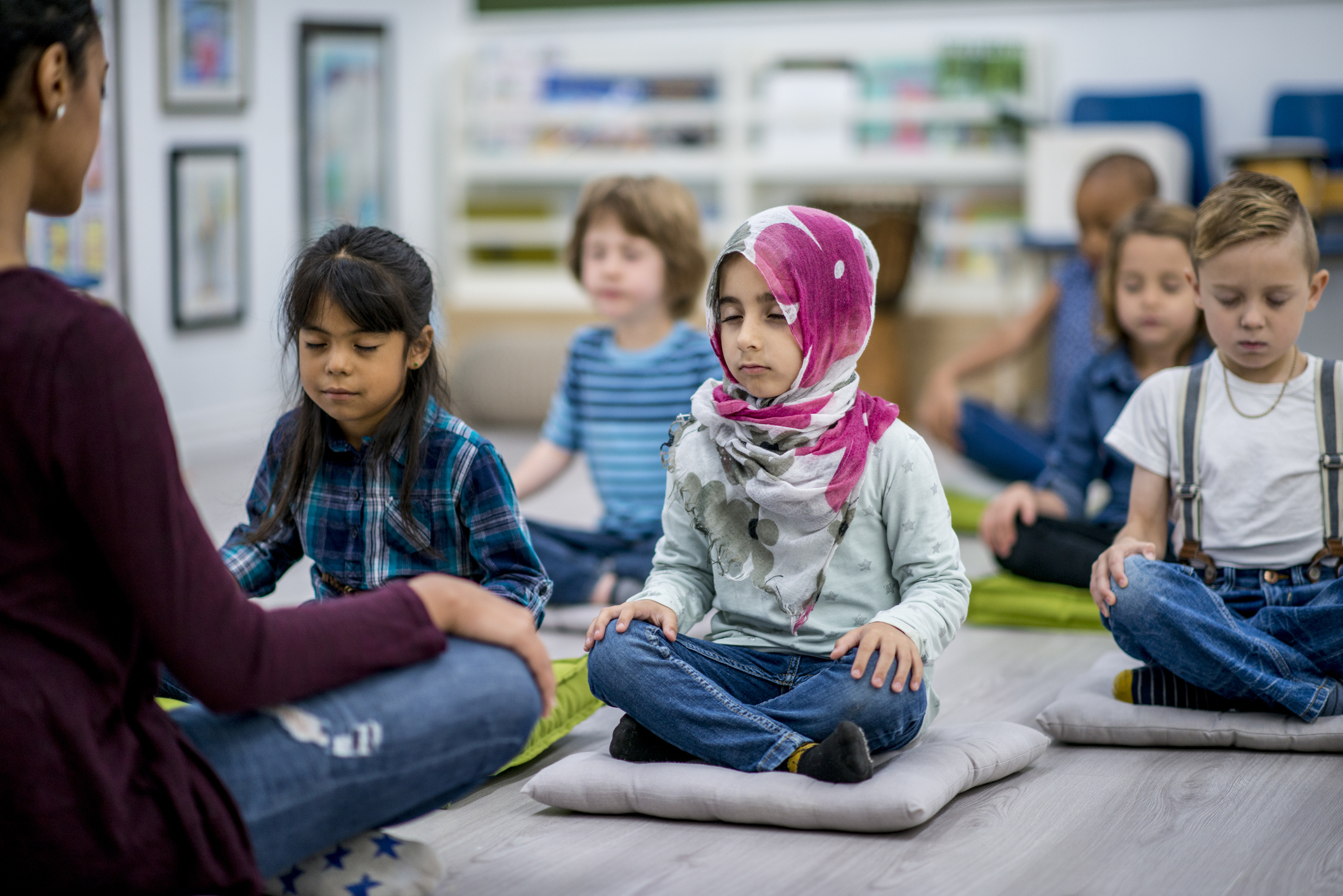 A teacher sitting on the floor with her students, practicing mindfulness techniques.