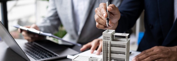 two people sitting at a desk with a laptop while pointing at a building mockup