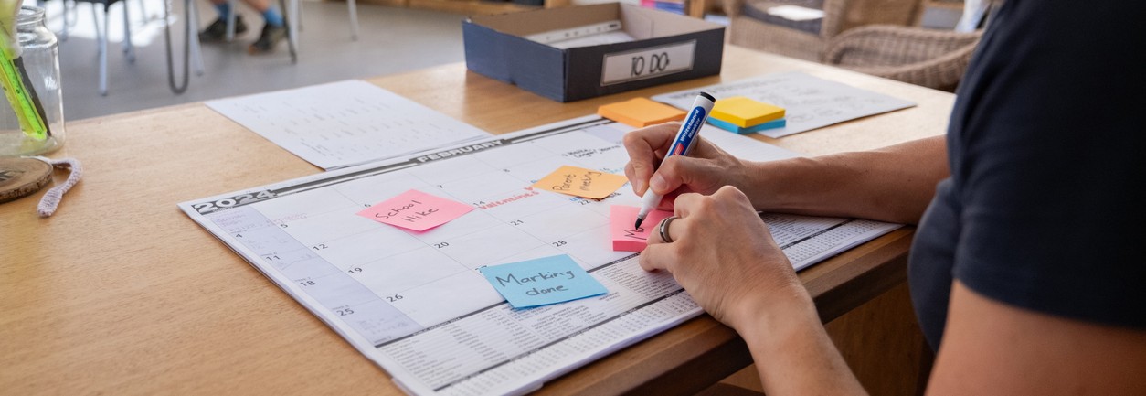 School teacher sits in her classroom and uses sticky adhesive notes to make reminders on her monthly calendar