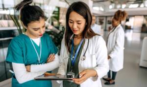 Two female doctors using digital tablet and talking in modern hospital corridor